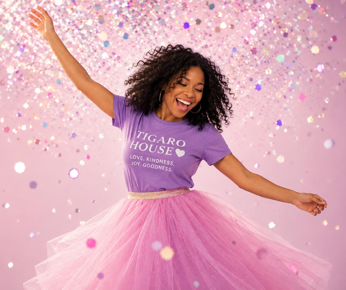 Tigaro House | Sharing Love, Kindness, Joy & Goodness Woman wearing a purple Tigaro House shirt celebrating joyfully, representing Tigaro House’s mission of sharing love, kindness, joy, and goodness.
